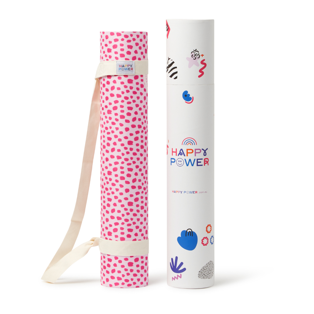 Eco friendly exercise and yoga mat rolled up with bonus carry strap. Mat features Bright pink dots on a pale pink background with a blue spot, a pink spot and pink petals.