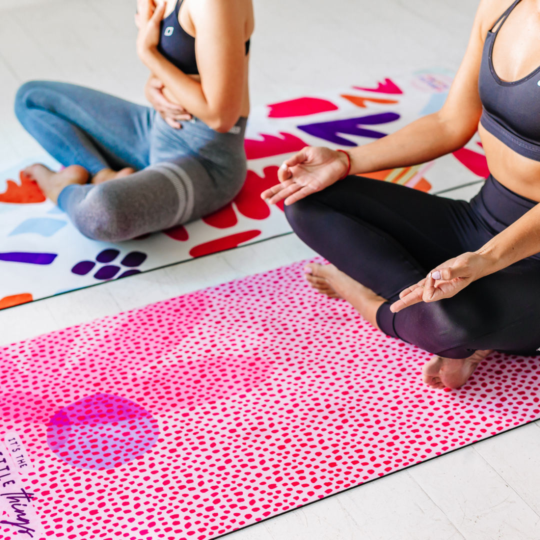 Two woman sit in yoga poses on non-slip colourful yoga mats.