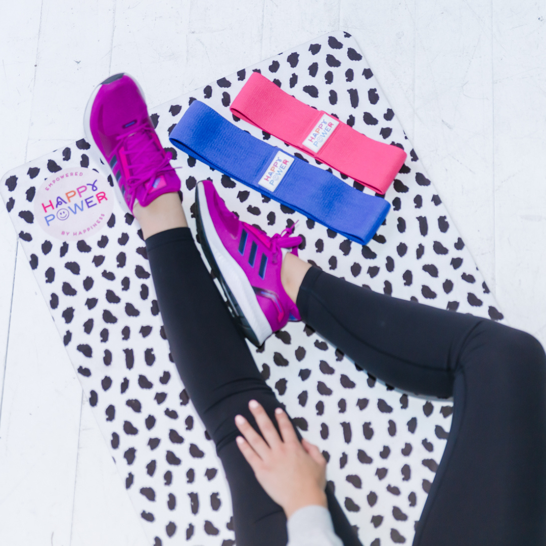 Eco friendly exercise and yoga mat with black feather dots on a white background. One blue and one pink resistance band placed on the non-slip mat.